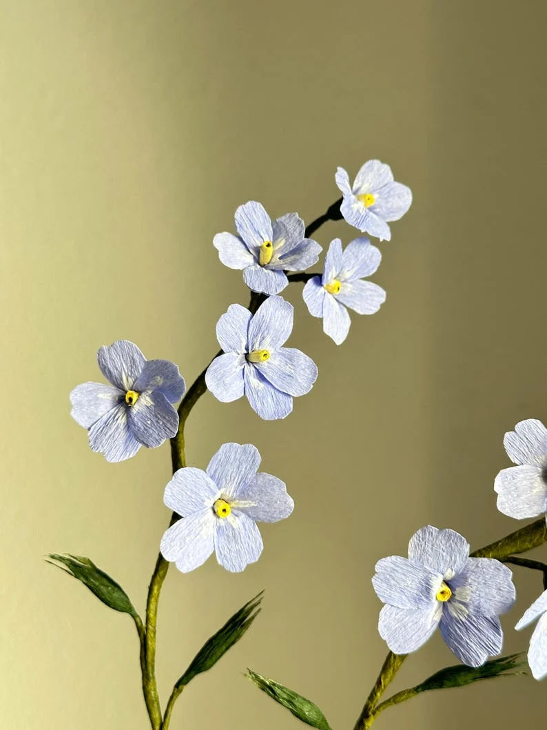 Nomeolvides azules hechos de papel crepé en una taza de té.