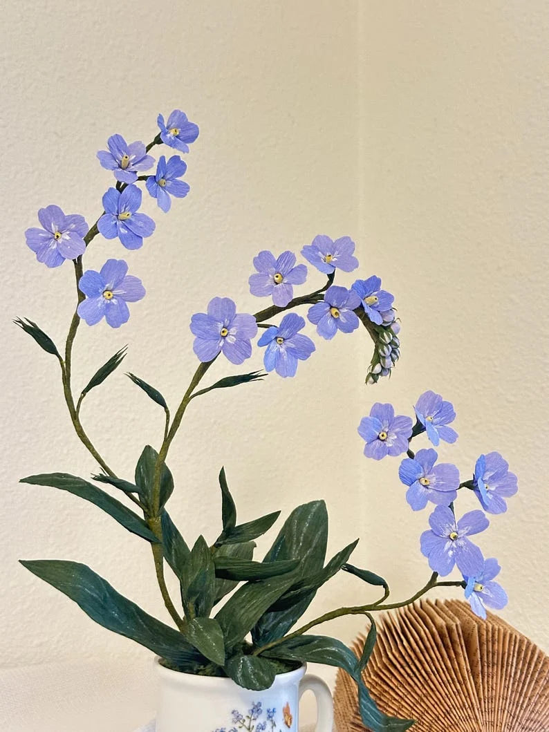 Nomeolvides azules hechos de papel crepé en una taza de té.